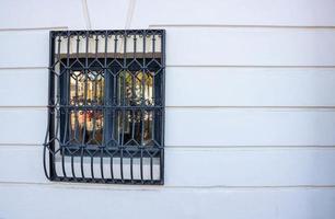 een klein Gesloten venster, verjaard met zwart metaal bars Aan de wit muur van de huis foto