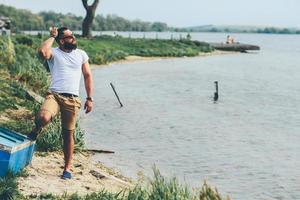 Amerikaanse bebaarde man met telefoon in de buurt van de rivier foto