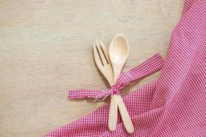 keuken gebruiksvoorwerpen. houten vork en lepel met rood kleding stof Aan houten achtergrond foto