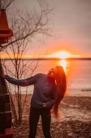 vrouw genieten van tijd ontspannende door de mooi meer Bij zonsopkomst. foto