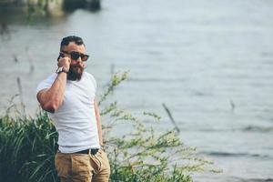 Amerikaanse bebaarde man met telefoon in de buurt van de rivier foto