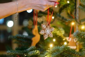 vrouw hand- blijft hangen een peperkoek sneeuwvlok Aan de Kerstmis boom foto