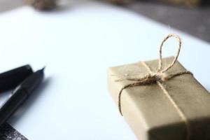 vakantie cadeaus Kerstmis en nieuw jaar geschenk doos verpakt in bruin papier, pijnboom kegels en wit papier en pennen geplaatst Aan de tafel, kopiëren ruimte. foto