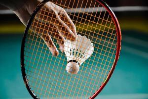 badminton racket en oud wit shuttle Holding in handen van speler terwijl portie het over- de netto vooruit, vervagen badminton rechtbank achtergrond en selectief focus foto