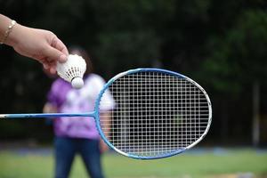 buitenshuis badminton spelen, zacht en selectief focus Aan wit shuttle, wazig Aziatisch vrouw en bomen achtergrond, concept voor buitenshuis badminton spelen in vrije tijd en dagelijks werkzaamheid. foto