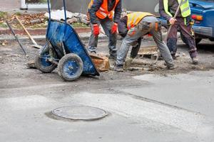 een team van weg arbeiders zijn repareren een riool mangat Aan de rijbaan. foto