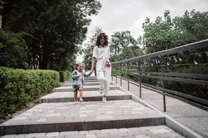 jong moeder en schattig weinig dochter wandelen naar beneden de straat foto