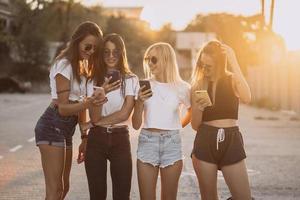 vier aantrekkelijk Dames zijn staand Aan auto parkeren met smartphones foto