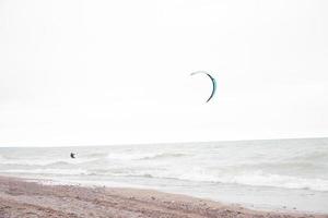 single vlieger surfer Aan stormachtig wateren van meer Michigan. zanderig strand Aan de kant. klein steentjes langs de kustlijn lijn. bewolkt bewolkt lucht. kleurrijk parachute. foto