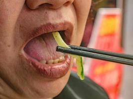 dichtbij omhoog senior Aziatisch vrouw mond gebruik eetstokje aan het eten groente foto