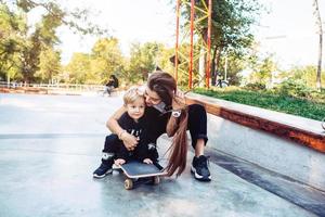 jong moeder geeft les haar weinig jongen naar rijden een skateboard foto