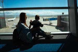 weinig jongen en zijn moeder zittend in een luchthaven foto