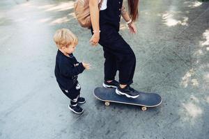 jong moeder geeft les haar weinig jongen naar rijden een skateboard foto