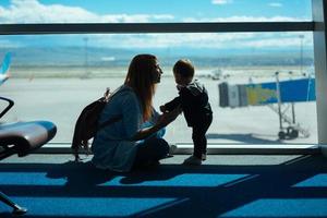 weinig jongen en zijn moeder zittend in een luchthaven foto