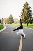 vrouw atleet springend salto Aan de weg, aan het doen opdrachten buitenshuis. foto