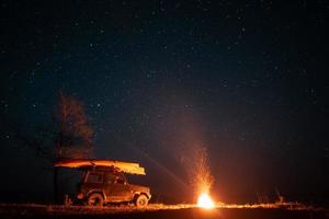 nacht landschap met helder kampvuur en auto foto