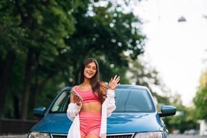 vrouw gebruik makend van mobiel telefoon in de buurt auto Bij de straat foto