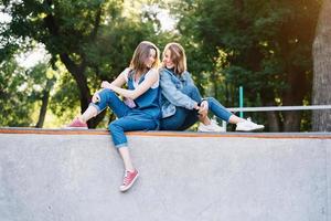 twee gelukkig jong meisjes zittend Bij de vleet park foto