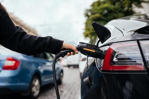 vrouw in de buurt elektrisch auto. voertuig opgeladen Bij de opladen station. foto