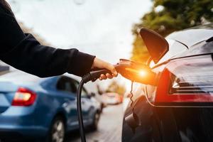 vrouw in de buurt elektrisch auto. voertuig opgeladen Bij de opladen station. foto