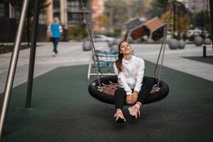 jong vrouw ritten Aan een schommel Bij de speelplaats. foto