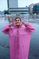 jong glimlachen vrouw in een roze regenjas genieten van een regenachtig dag. foto