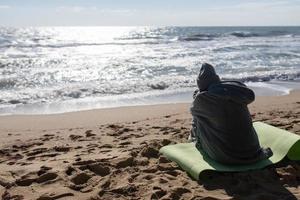 mooi vrouw in warm kleren zittend Aan de verkoudheid herfst strand. foto