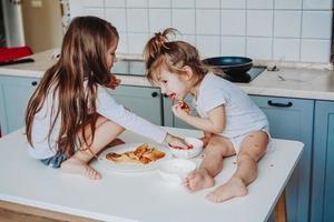 twee weinig meisjes in de keuken zittend Aan de tafel. foto