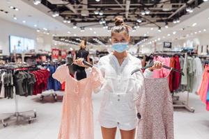 jong vrouw boodschappen doen kleding in kleding winkel met beschermend gezicht masker foto