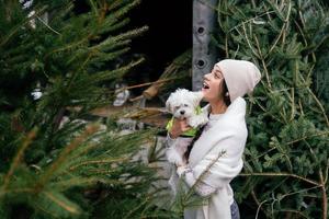 vrouw met een wit hond in haar armen in de buurt een groen Kerstmis bomen foto