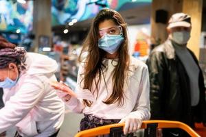 vrouw met de chirurgisch masker en de handschoenen is boodschappen doen in de supermarkt foto