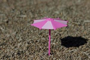 speelgoed- paraplu met een schaduw van de zon Aan een rotsachtig strand, kust. de concept van een plaats onder de zon. foto