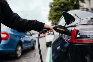 vrouw in de buurt elektrisch auto. voertuig opgeladen Bij de opladen station. foto