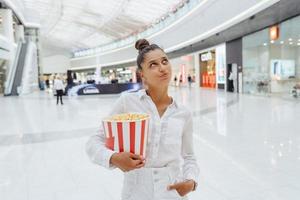 jong schattig vrouw Holding popcorn in de winkelcentrum achtergrond foto