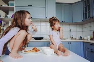 twee weinig meisjes in de keuken zittend Aan de tafel. foto