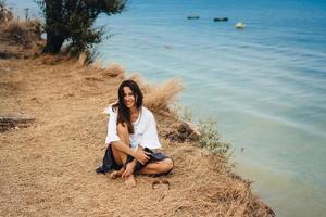 aantrekkelijk vrouw in zomer rok en overhemd zit Aan de kust foto