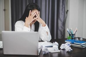 spanning bedrijf vrouw persoon van moeilijk werk, depressie in kantoor. moe en angstig werknemer vrouw met ongelukkig Bij probleem functie. jong zakenvrouw zittend verdrietig voorkant van laptop computer Aan bureau. foto