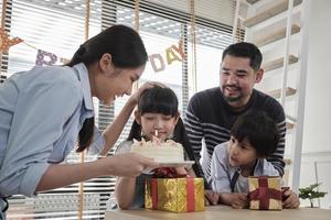 gelukkig Aziatisch Thais familie, jong dochter is verrast, verjaardag taart en lief geschenk, meisje slagen kaars, bidden en vrolijk viert partij met ouders samen, speciaal huiselijk huis evenement levensstijl. foto