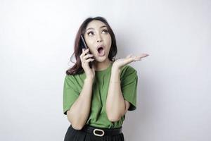 geschokt Aziatisch vrouw vervelend een groen t-shirt richten Bij de kopiëren ruimte ondersteboven haar Holding haar telefoon, geïsoleerd door een wit achtergrond foto