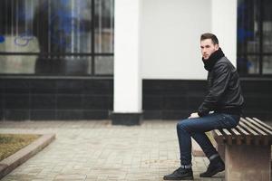 een Mens gekleed in jeans en zwart jasje stoelen Aan een bank foto