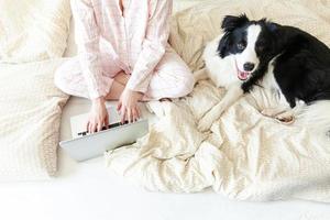 mobiel kantoor Bij huis. jong vrouw in pyjama zittend Aan bed met huisdier hond werken gebruik makend van Aan laptop pc computer Bij huis. levensstijl meisje aan het studeren binnenshuis. freelance bedrijf quarantaine concept. foto