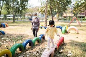 schattig Aziatisch meisje en moeder glimlach Speel Aan school- of kleuterschool werf of speelplaats. gezond zomer werkzaamheid voor kinderen. weinig meisje beklimming buitenshuis speelplaats. kind spelen buitenshuis speelplaats. foto