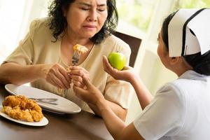 verpleegster suggereren volwassen vrouw geduldig naar eten appel in plaats daarvan van kip gebakken. foto