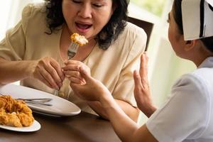 verpleegster verbiedend volwassen vrouw geduldig naar eten kip gebakken in de kamer. foto