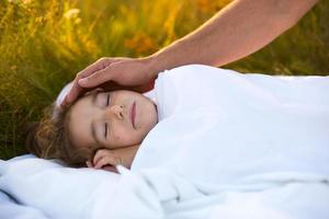 meisje slaapt Aan wit bed in de gras, vers lucht. van vader hand- voorzichtig klopt zijn hoofd. zorg, bescherming, Internationale kinderen dag, mug bijt foto