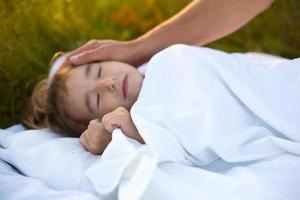 meisje slaapt Aan wit bed in de gras, vers lucht. van vader hand- voorzichtig klopt zijn hoofd. zorg, bescherming, Internationale kinderen dag, mug bijt foto