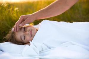 meisje slaapt Aan wit bed in de gras, vers lucht. van vader hand- voorzichtig klopt zijn hoofd. zorg, bescherming, Internationale kinderen dag, mug bijt foto