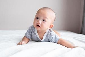 portret baby in een gestreept shirt, voorkant visie, kruipen Aan een wit matras foto