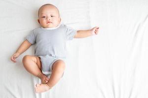 de top visie beeld heeft een kant Oppervlakte , is een baby jongen vervelend een gestreept shirt. liggen met uw poten omhoog en uw armen uitgestrekt Aan de bed. foto