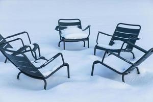 stoelen buitenshuis in park gedekt met dik laag van wit sneeuw. metaal tuin meubilair gedurende winter het weer. buitenshuis meubilair na sneeuwstorm. straat restaurant stoelen foto